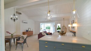 Amplia sala de estar con una mesa de comedor, sillas, un sofá y un sillón colgante. Hay una isla grande con cajones y un lámpara colgante sobre ella.