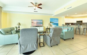 A living room with two sofas, a TV, a ceiling fan, and a kitchen area with a microwave. - The Gulf Is Calling –Lazy River Getaway Phoenix West 1204 (Orange Beach)