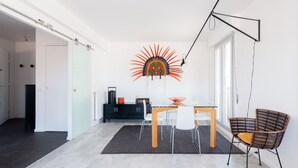 A modern dining area with a glass table, white chairs, a black and brown woven chair, a decorative wall piece, and a black cabinet.