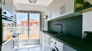 A modern kitchen with a washing machine, a sink, and a view of buildings outside.