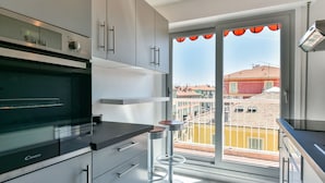 A modern kitchen with a large oven, a window with a view of buildings, and a balcony with a railing.