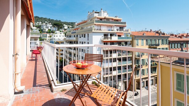 A balcony with a table and chairs, a red chair, and a basket of fruit.
