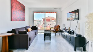 A modern living room with a sofa, a coffee table, a TV, and a view of the city through large windows.