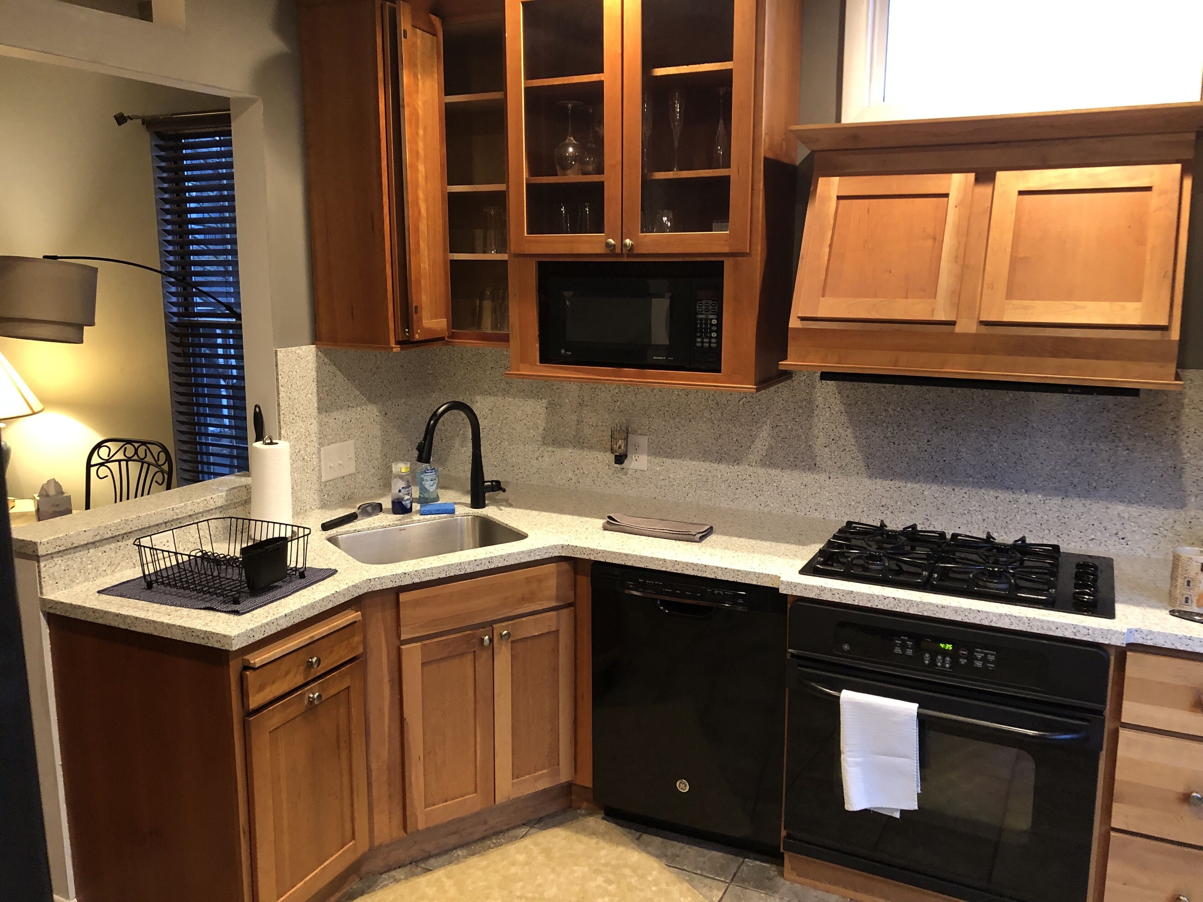 A kitchen with wooden cabinets, a stainless steel sink, a black dishwasher, a black stove, and a microwave.