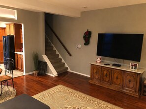 Una sala de estar con escalera, televisor, aparador y planta.