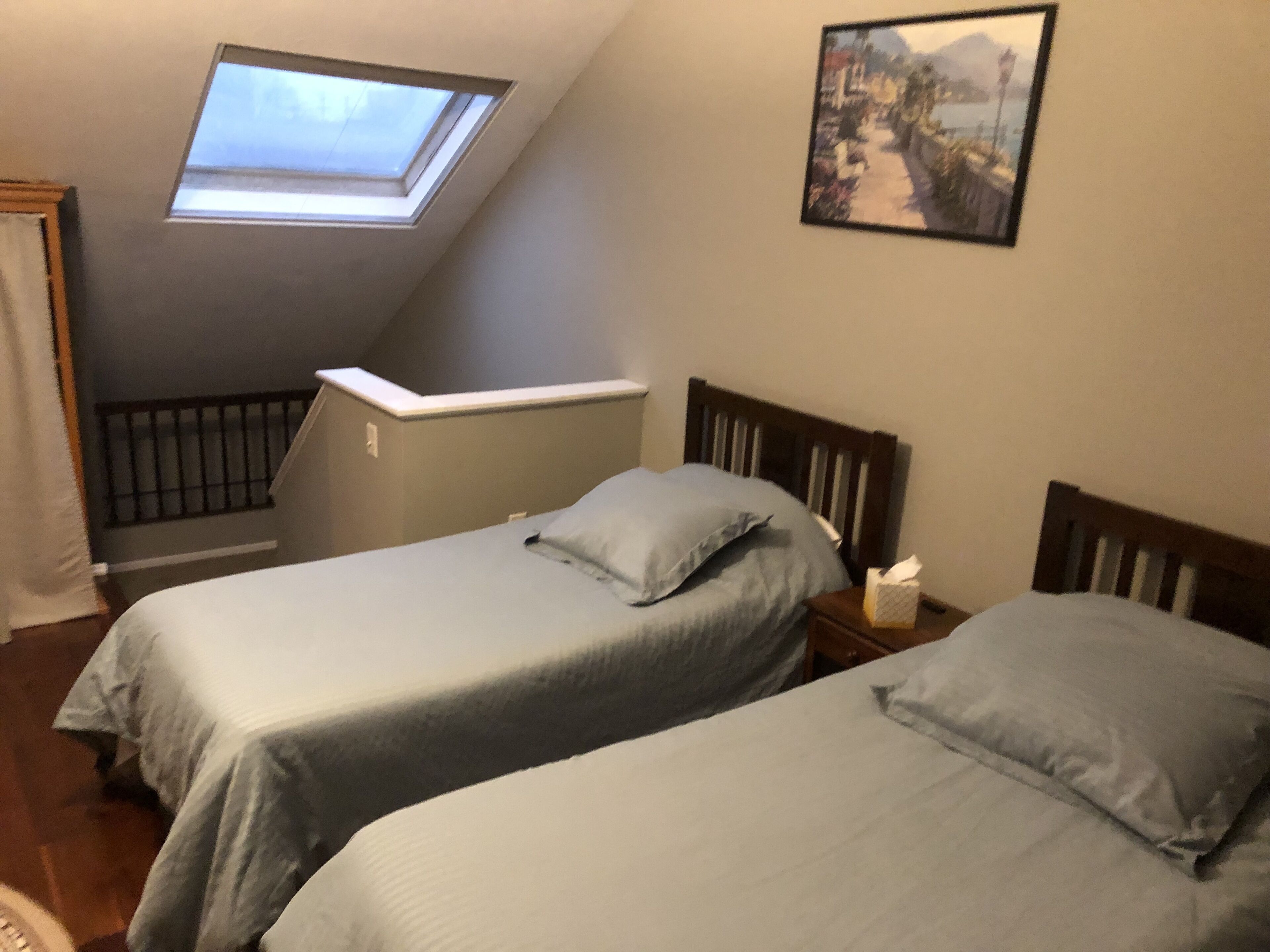 Ein Schlafzimmer mit zwei Betten, einem Oberlicht, einem Gemälde und einem kleinen Nachttisch.