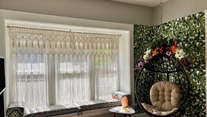 Una habitación con un asiento junto a la ventana, una silla colgante y un muro decorado con un diseño de hojas.