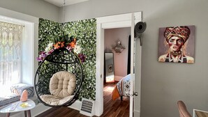 Una habitación con suelo de madera, una silla colgante, una mesita con una lámpara de sal y un cuadro en la pared.