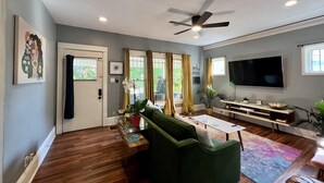 Una sala de estar moderna con un sofá verde, una mesa de centro, un televisor de pantalla plana y un ventilador de techo.