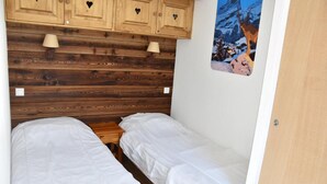 Een kleine, knusse kamer met twee eenpersoonsbedden, een houten hoofdbord en een schilderij van een besneeuwd berglandschap.