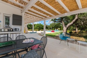 A covered outdoor dining area with a pool and garden in the background. - VILLA WITH A TRULLO AND A POOL, SURROUNDED BY OLIVE GROVES (San Vito dei Normanni)