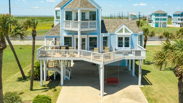 A two-story beach house with a balcony, a swing, and a view of the ocean. - 2nd row Gulf Views w/ Large Deck, Open Living, Private Bedrooms - Cool & Coastal (Galveston)