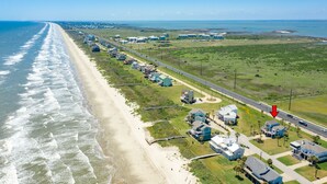 A coastal residential area with houses along a beachfront, a road with a traffic sign, and a clear view of the ocean. - 2nd row Gulf Views w/ Large Deck, Open Living, Private Bedrooms - Cool & Coastal (Galveston)