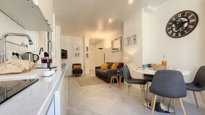 A modern kitchen with a dining area, a sofa, and a large wall clock. - N&J - L'ANCRE - Port district - Close Old Town (Niza)