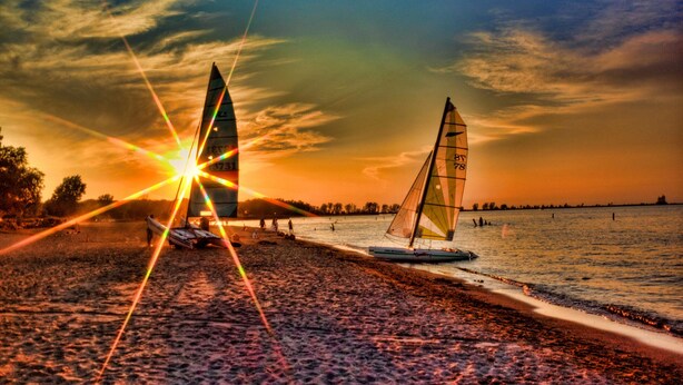 Una playa con dos veleros y un atardecer de fondo.