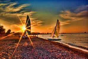 Ein Strand mit zwei Segelbooten und einem Sonnenuntergang im Hintergrund.