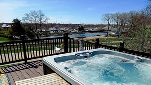 Un jacuzzi en una terraza de madera con vista a un puerto deportivo y barcos al fondo.