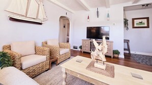 Una sala de estar con muebles de mimbre, una mesa de centro de madera, un televisor y un modelo de velero.