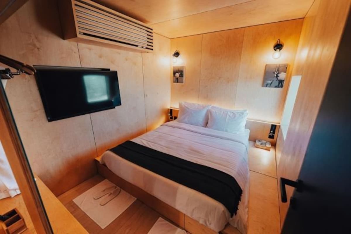A bedroom with a bed, a mounted television, wall-mounted lights, and a wooden headboard.
