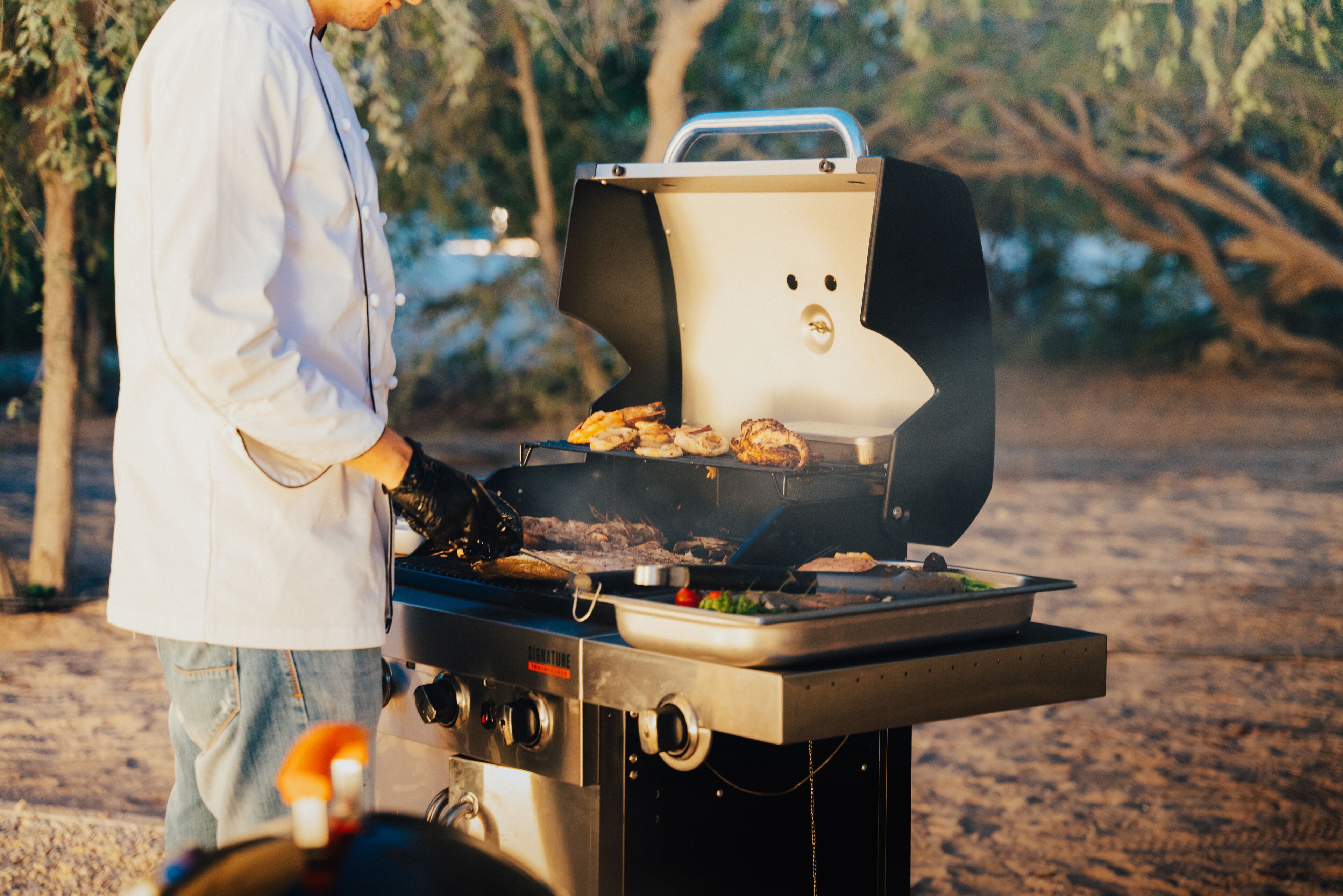 Una persona asando comida en una parrilla al aire libre con una pantalla digital y perillas de control.