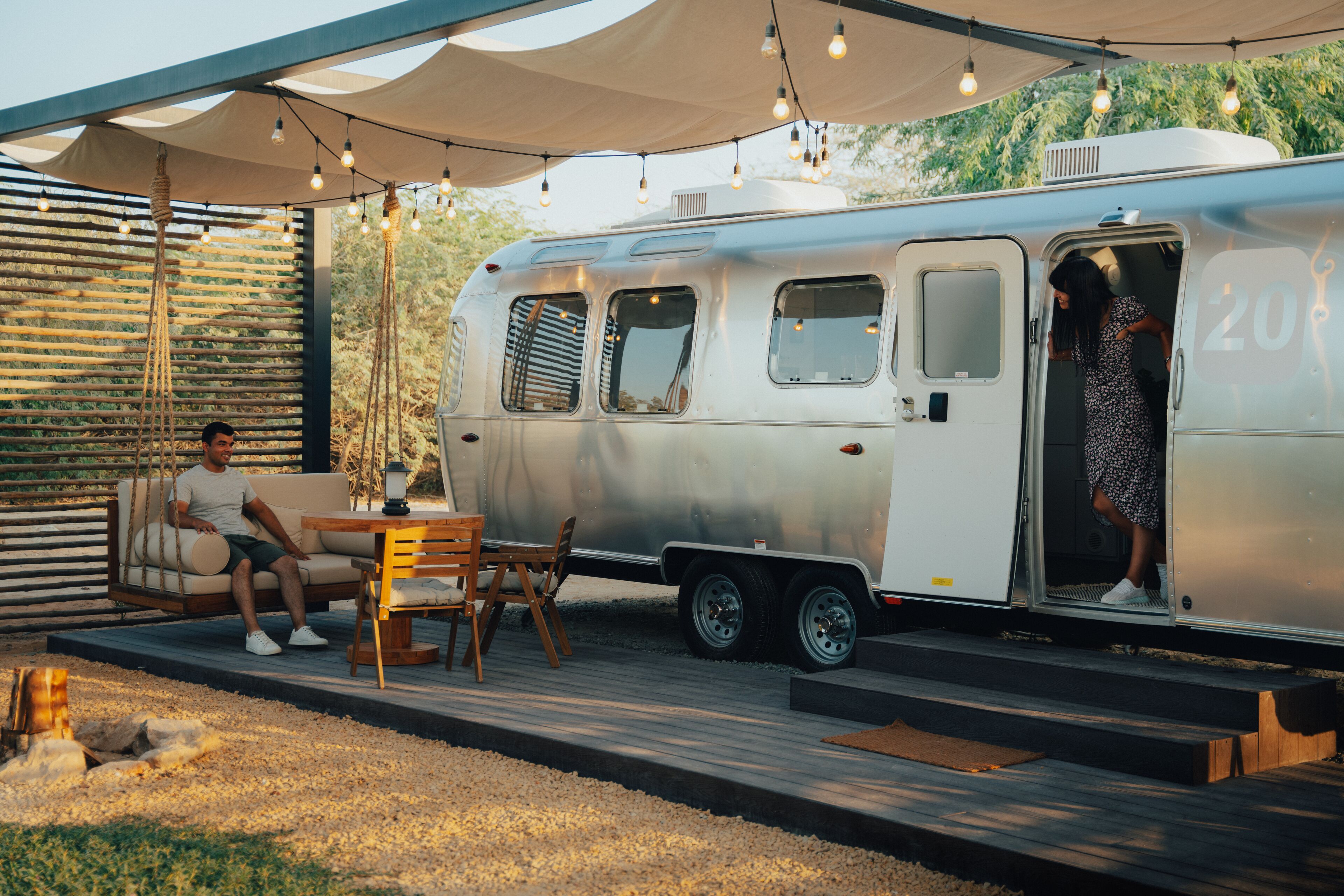 A vintage camper with a covered deck, seating area, and a person standing at the entrance.