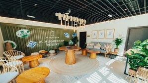 A modern, well-lit lounge area with round wooden tables and comfortable seating, featuring a green wall with the resort's logo and name. -  Bab Al Nojoum Al Mugheirah (Al Mirfa)
