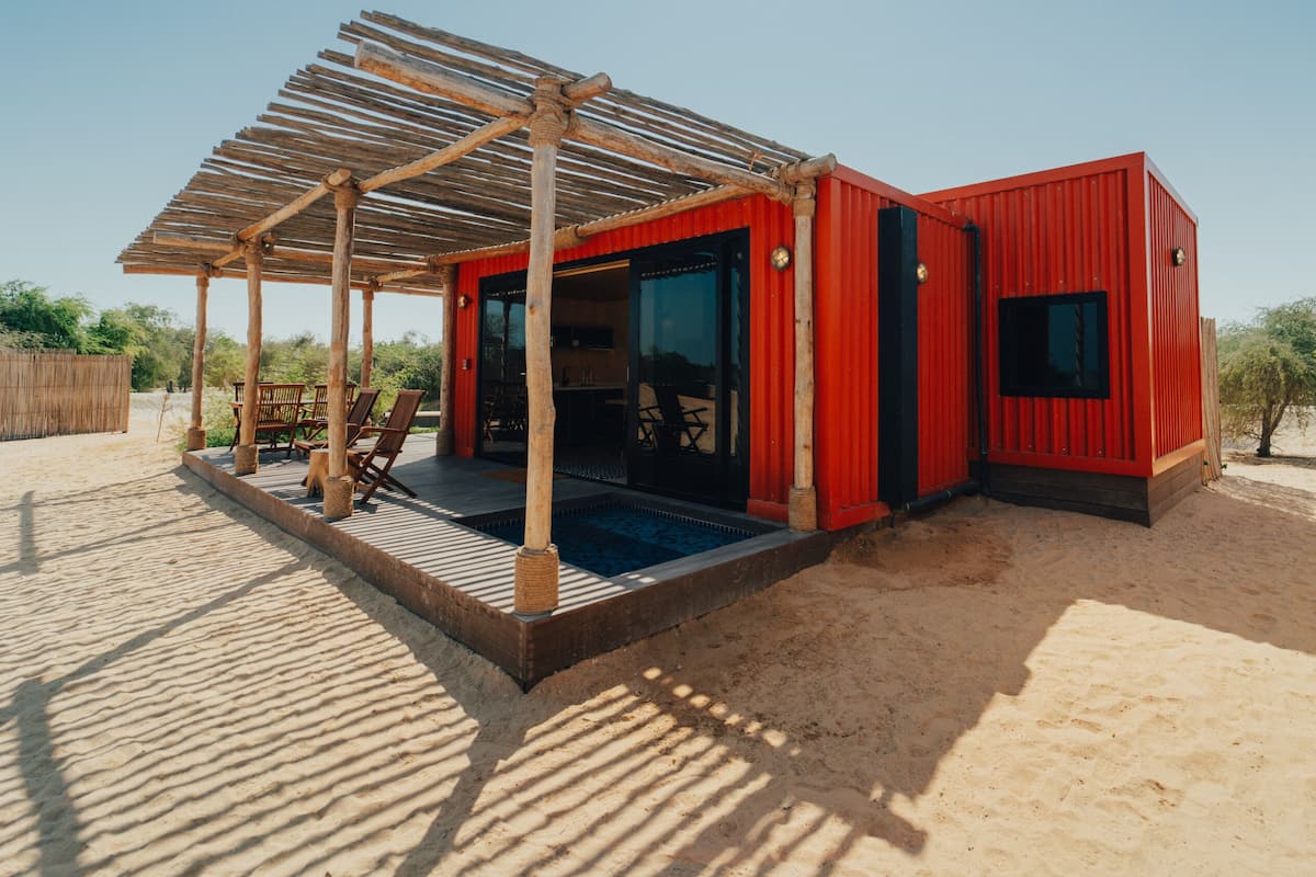A red building with a pool, wooden deck, and outdoor seating.