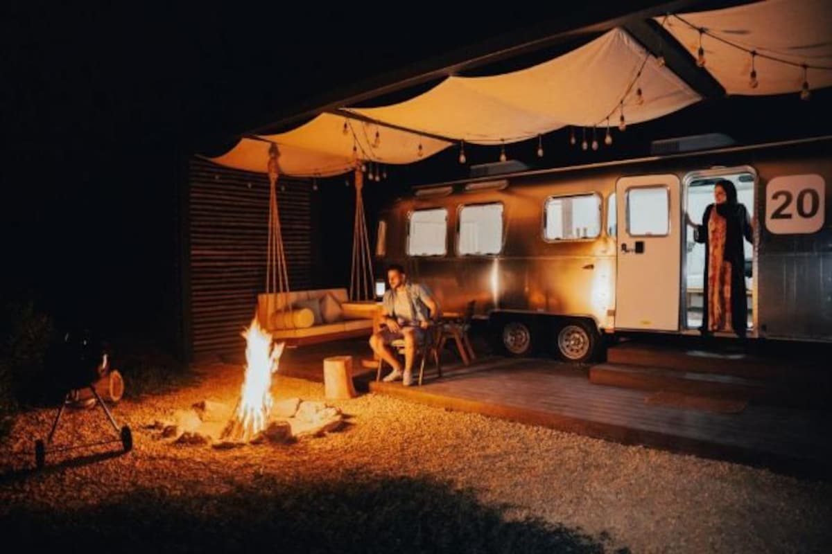 A camper with a fire pit, a covered seating area, and a person standing by the entrance.
