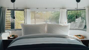 Un lit avec du linge de lit blanc, deux lampes suspendues et une fenêtre avec des rideaux.
