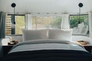 A bed with white linens, two hanging light bulbs, and a window with curtains. -  Bab Al Nojoum Al Mugheirah (Al Mirfa)