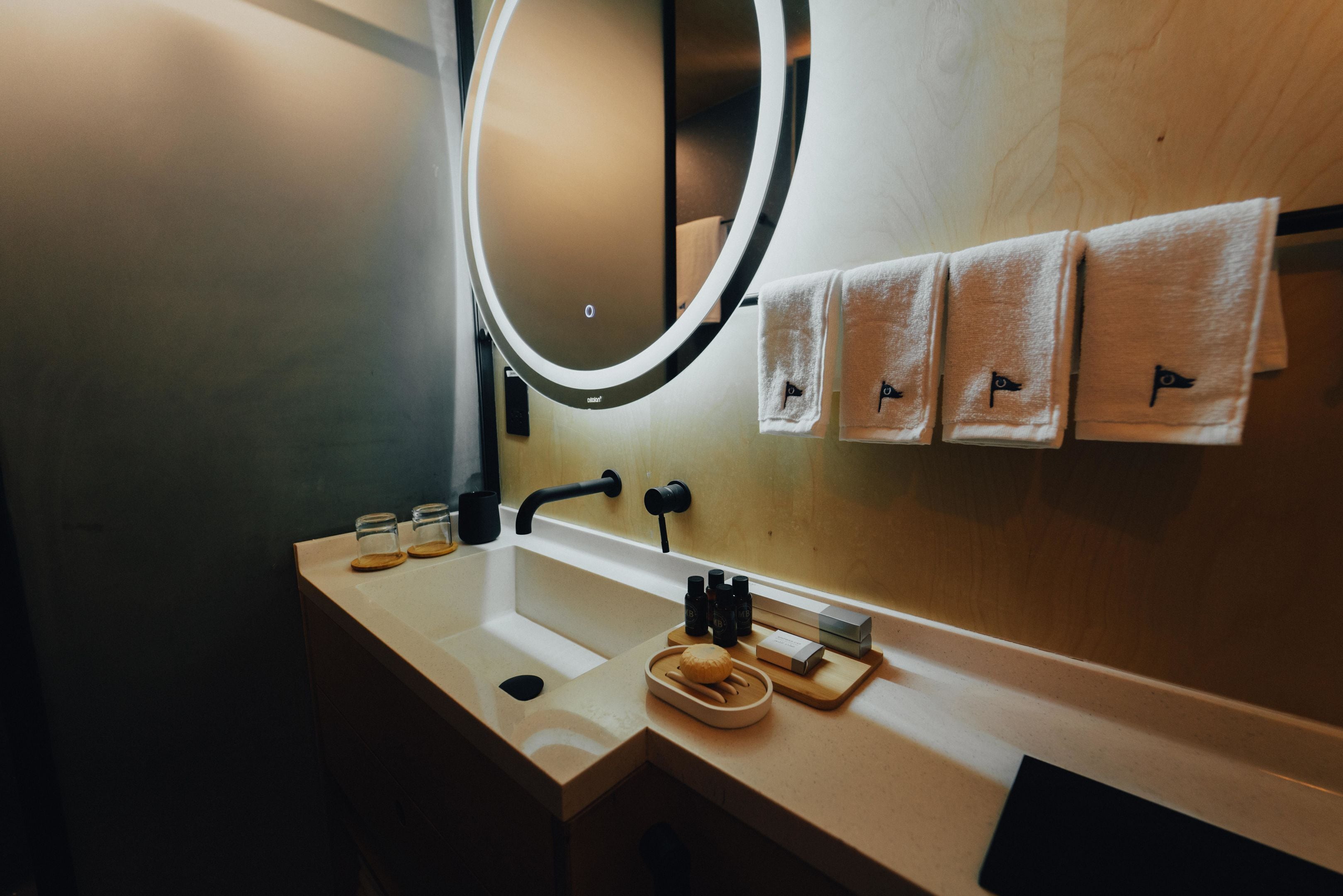 Une salle de bain avec un miroir rond, un lavabo et trois serviettes suspendues à un porte-serviettes.