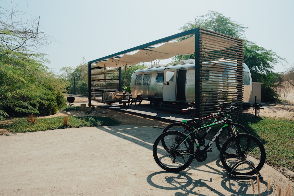 A camper with a covered outdoor seating area and a bicycle parked nearby.