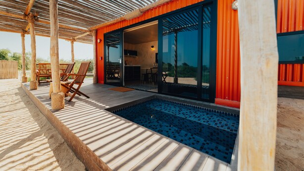 A modern outdoor pool area with wooden deck and lounge chairs, connected to a building with large glass doors and a red exterior. -  Bab Al Nojoum Al Mugheirah (Al Mirfa)