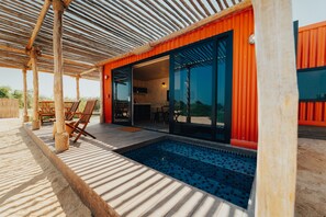 A modern outdoor pool area with wooden deck and lounge chairs, connected to a building with large glass doors and a red exterior. -  Bab Al Nojoum Al Mugheirah (Al Mirfa)
