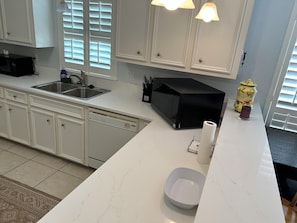 A kitchen with white cabinets, a black microwave, a sink, and a yellow canister.