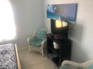 A room with a bed, a chair, a TV, and a painting on the wall.