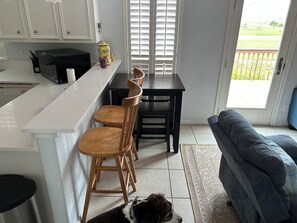 A kitchen with a white countertop, wooden chairs, a dining table, and a dog on the floor. - BayFront with Ocean View (Galveston)
