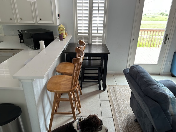 A kitchen with a white countertop, wooden chairs, a dining table, and a dog on the floor.