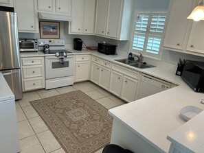 A kitchen with white cabinets, a stainless steel refrigerator, a toaster oven, a kettle, a coffee maker, and a dishwasher. - BayFront with Ocean View (Galveston)