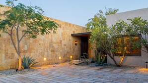 A courtyard with a paved walkway, a stone wall, and a building entrance with a door and window. - Luxury Ocean View Villa w/ Heated Pool, Hot Tub & Steps to Beach in Ritz Complex (San Jose Del Cabo)