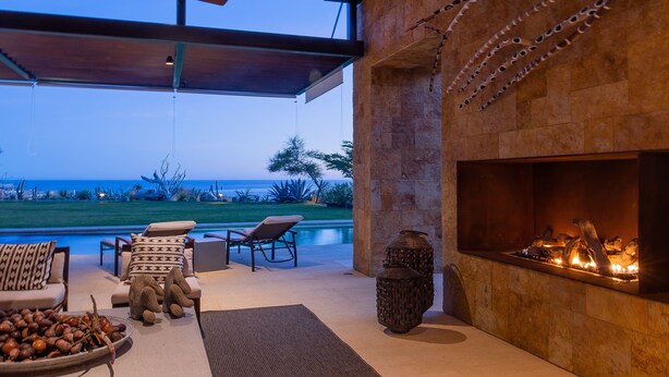 A modern outdoor lounge area with a fireplace, lounge chairs, and a view of the ocean. - Luxury Ocean View Villa w/ Heated Pool, Hot Tub & Steps to Beach in Ritz Complex (San Jose Del Cabo)