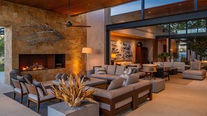 A modern outdoor living area with a stone fireplace, comfortable seating, and a view into the interior. - Luxury Ocean View Villa w/ Heated Pool, Hot Tub & Steps to Beach in Ritz Complex (San Jose Del Cabo)