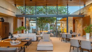 A spacious indoor area with a large dining table, multiple seating arrangements, and a view of the outdoors through large windows. - Luxury Ocean View Villa w/ Heated Pool, Hot Tub & Steps to Beach in Ritz Complex (San Jose Del Cabo)