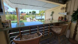 A bar area with wicker chairs, a glass-top table, and a view of a landscaped garden.