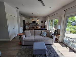 A modern living room with a sofa, a coffee table, and a view of the kitchen and outdoor area. - Indian Bayou Lake House 2 - Lakeside Oasis (Fort Myers Beach)
