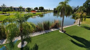 A serene landscape with a pond, palm trees, and a well-maintained lawn.