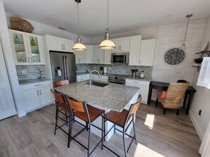 A modern kitchen with a central island, bar stools, a microwave, and a clock on the wall.