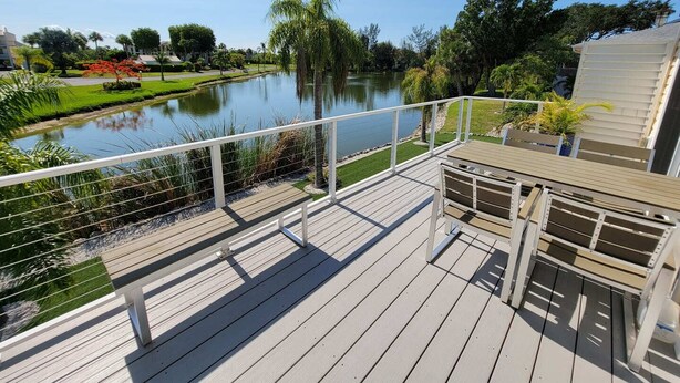 A wooden deck with a railing overlooking a calm lake, surrounded by greenery and trees.
