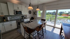 A modern kitchen with a central island, stainless steel appliances, and a large window offering a view of a landscaped area.