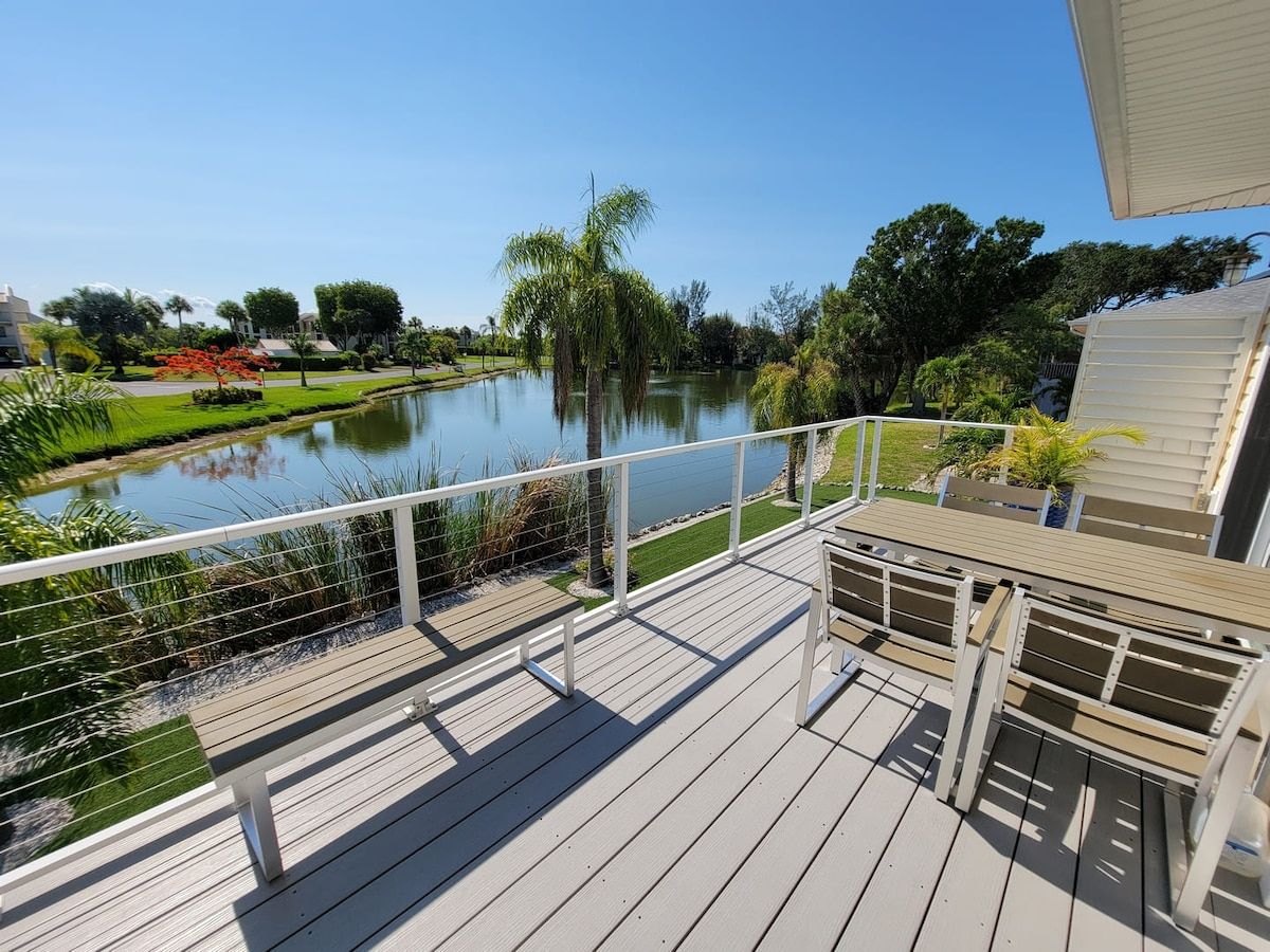 A wooden deck with a railing overlooking a calm lake and a landscaped garden.